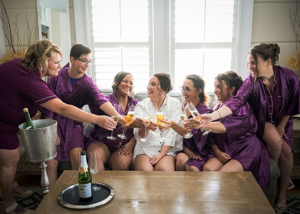 A group in matching purple robes toasts with champagne glasses while sitting together by bright windows.