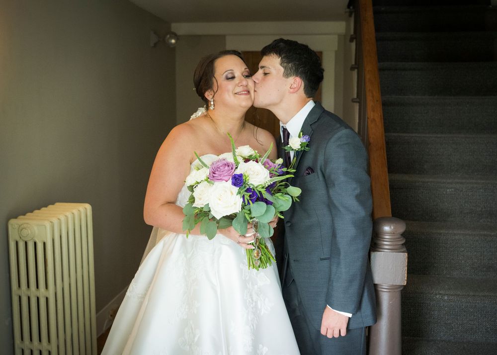 A couple shares a tender moment on their wedding day while holding a white and pink floral bouquet.