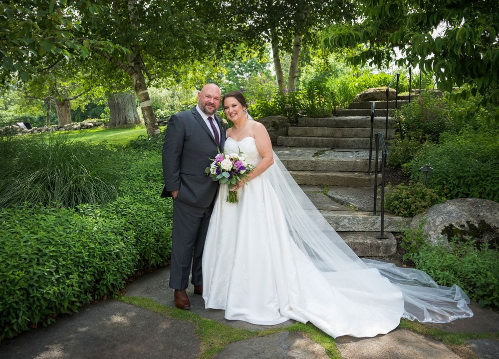 A romantic wedding photoshoot in a lush garden setting with white dress, flowers and stone steps in the background.