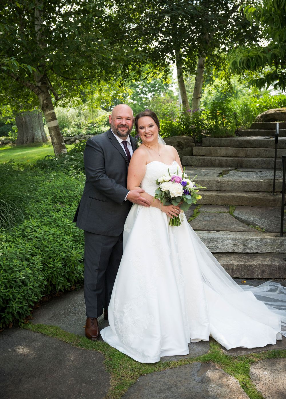Wedding couple shares intimate moments in a lush garden setting with stone steps and greenery as their backdrop.