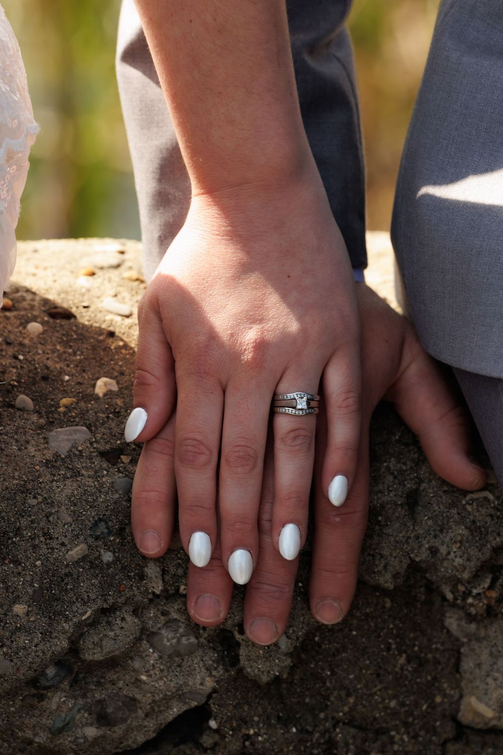 Two hands wearing wedding rings press into dark soil, symbolizing growth and unity in marriage.