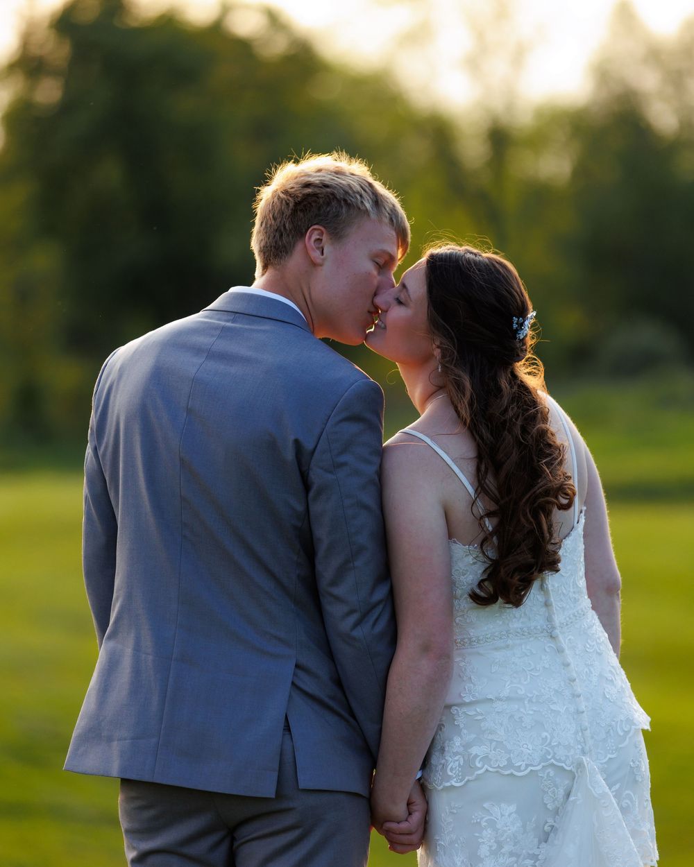 A romantic sunset moment with a couple in wedding attire embracing in a lush green field.