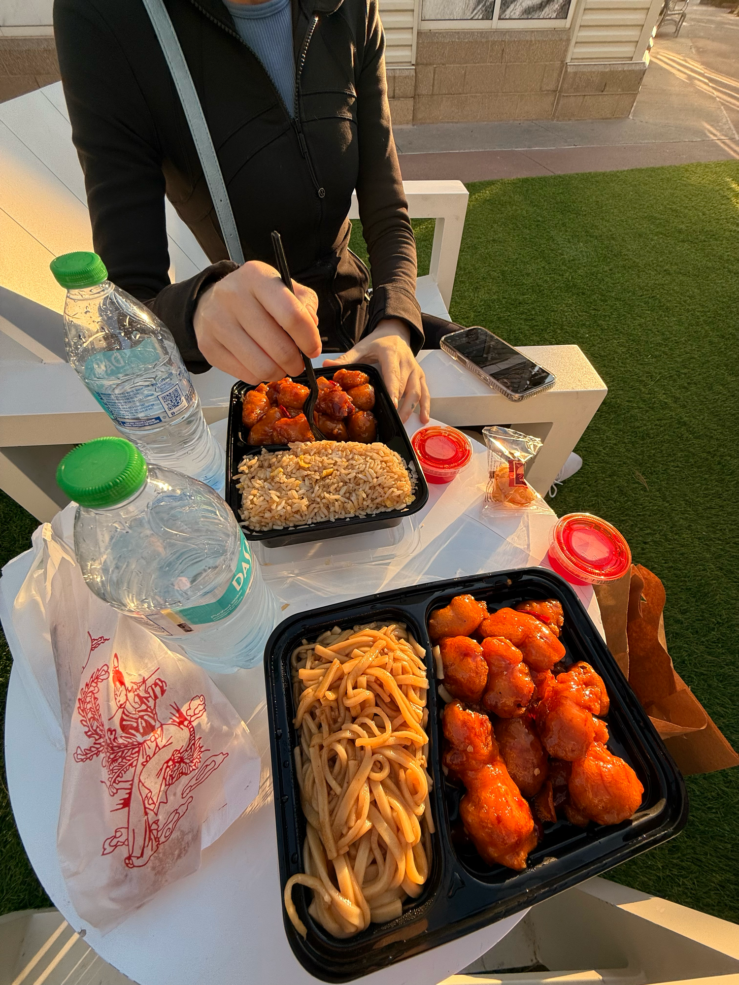 Take-out food containers with orange chicken, noodles and other Asian dishes on a table.