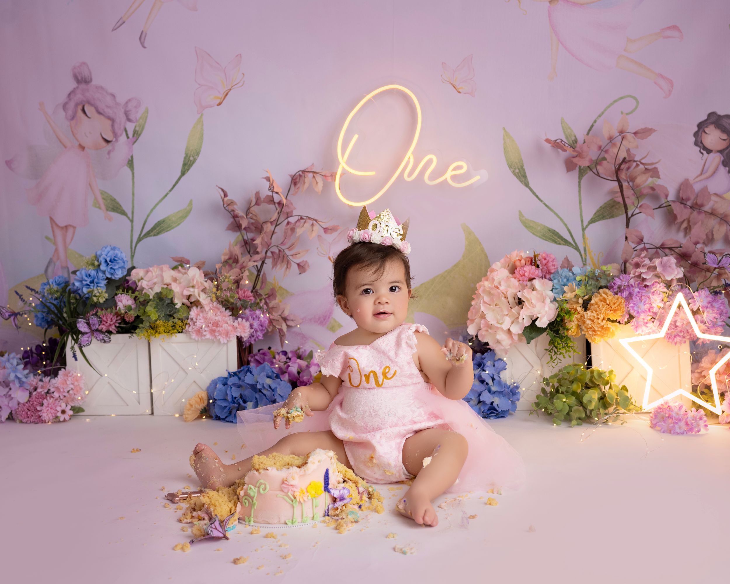 One year birthday scene with floral arrangements, neon lighting, and pink decor.