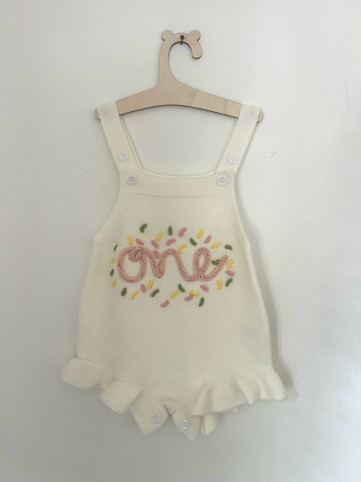 White baby romper with delicate pink embroidered floral design and ruffle details on straps.