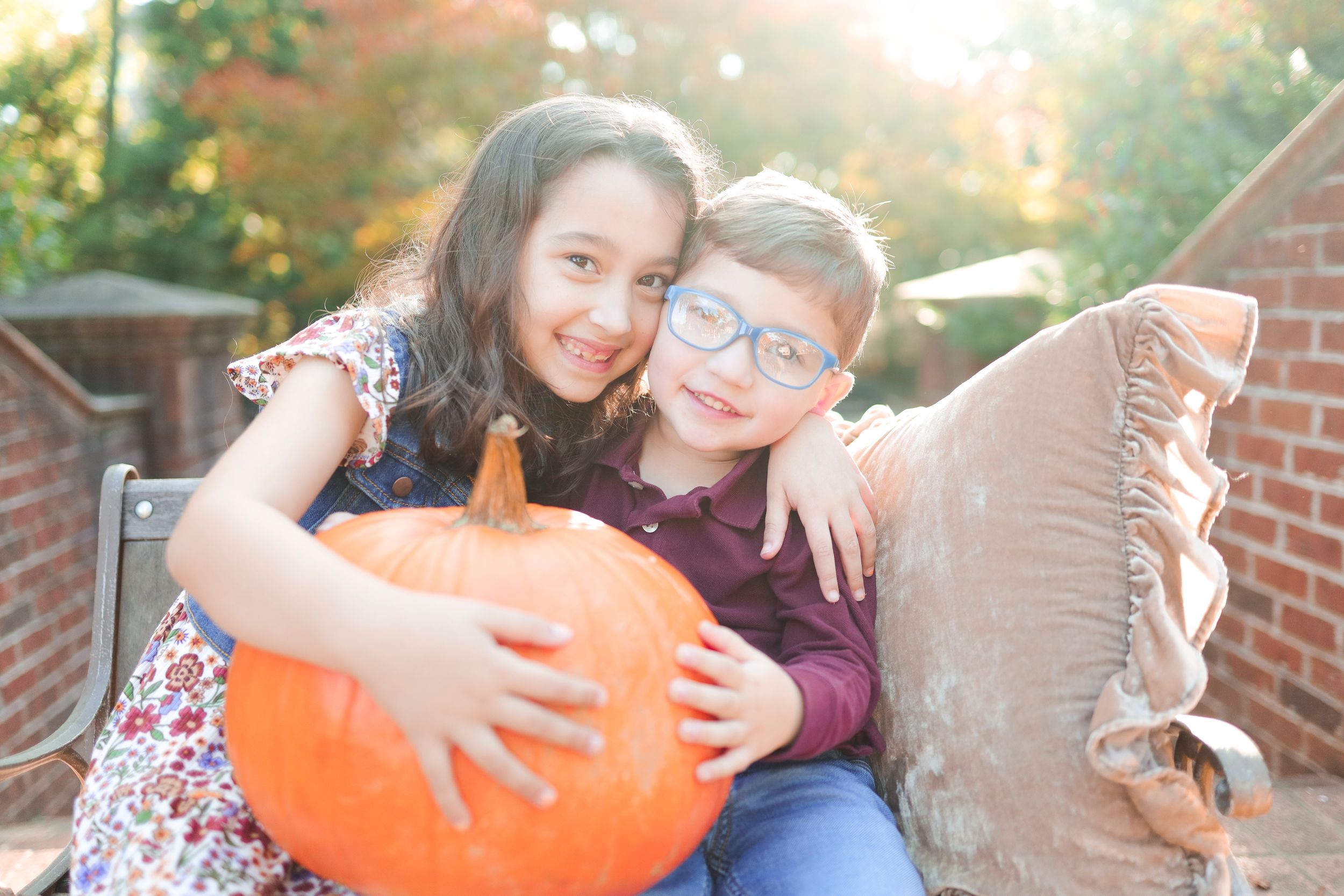 Two friends smile together while holding a large orange pumpkin outdoors during autumn.