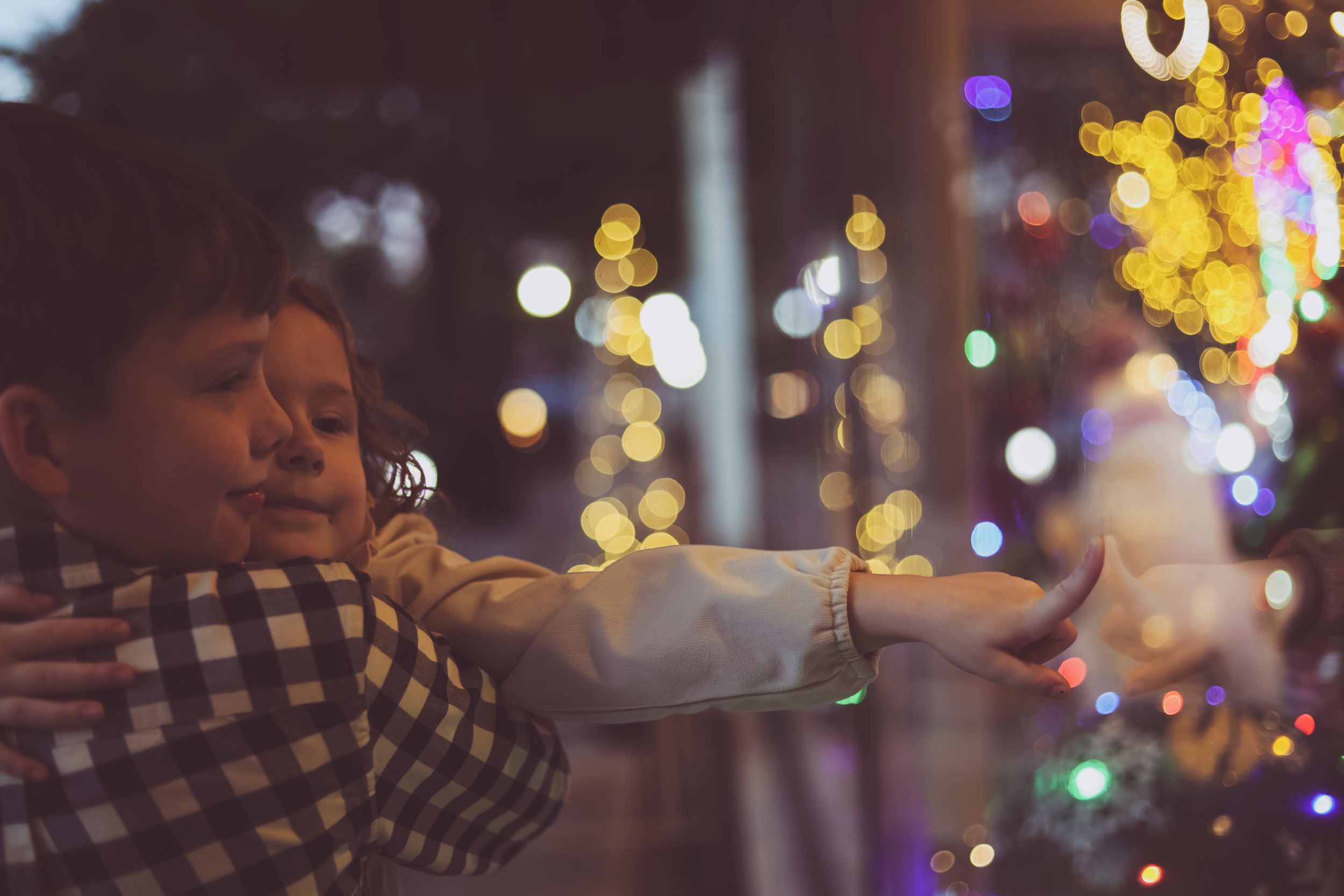 Child in checkered shirt gazes at glowing Christmas lights and decorations creating a magical holiday scene.