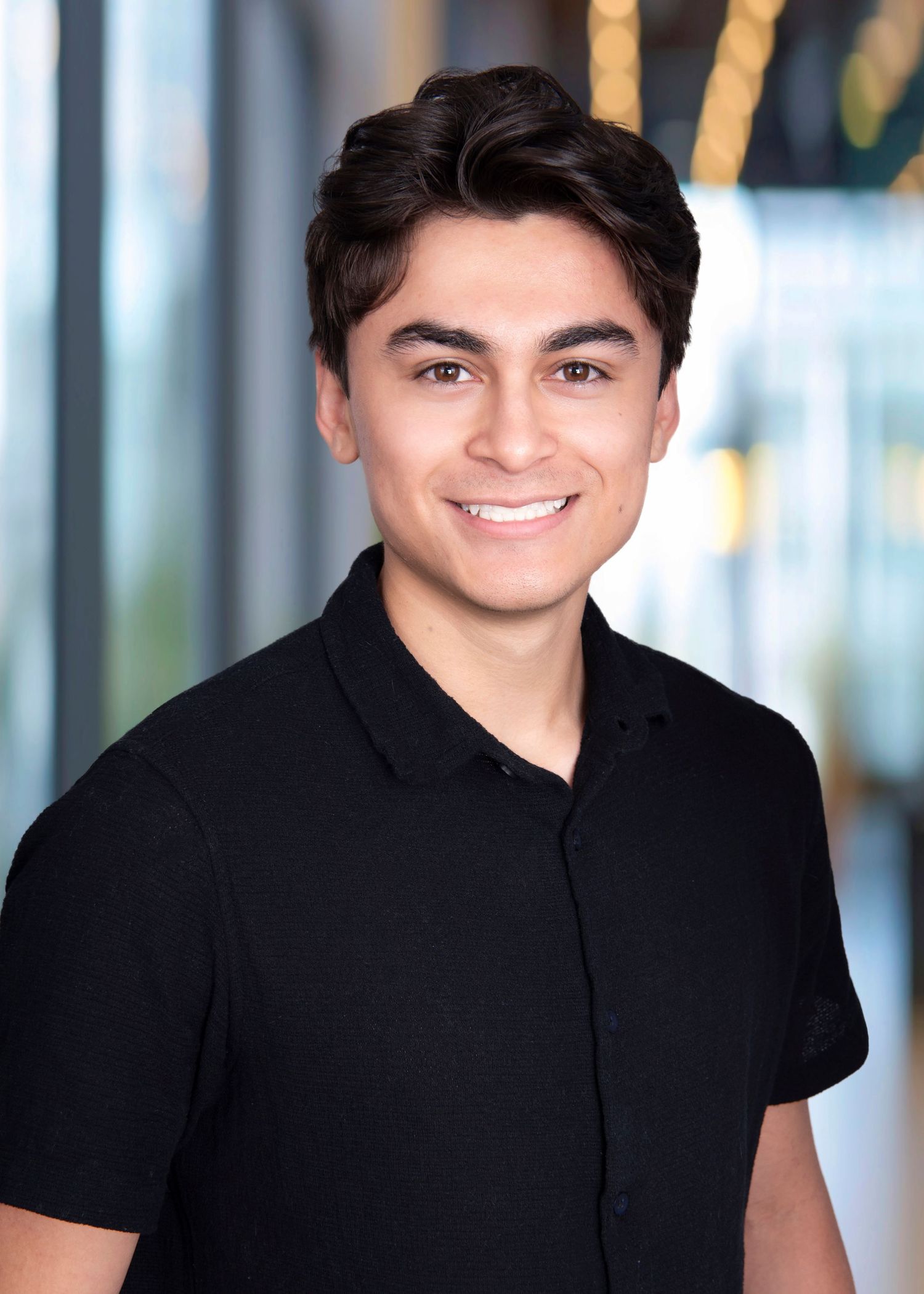 Professional headshot of a smiling young man wearing a black polo shirt against a blurred background.
