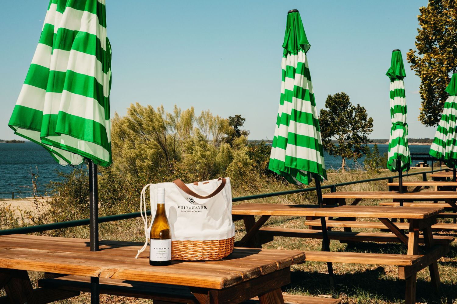 Green and white striped beach umbrellas lined up along wooden picnic tables by the shore.