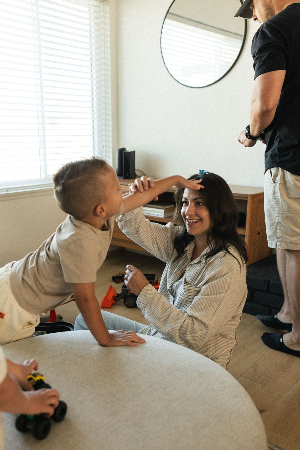 Family playtime scene in a bright living room with round mirror and windows.