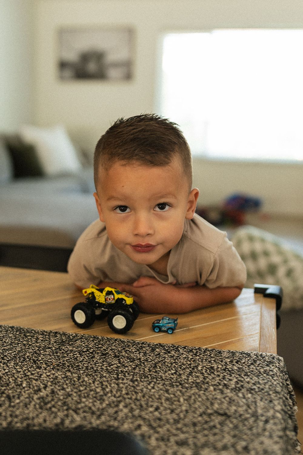 A toy monster truck and small car being played with on wooden coffee table in living room.
