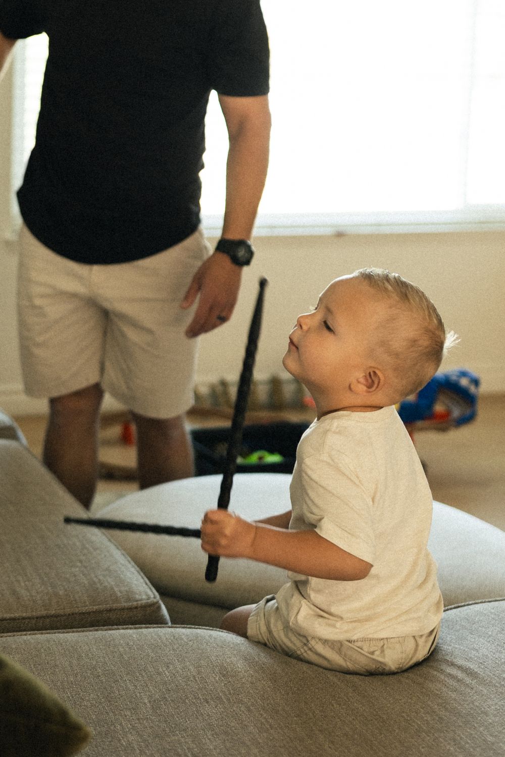 Child sitting on gray couch playing with a stick-like toy.