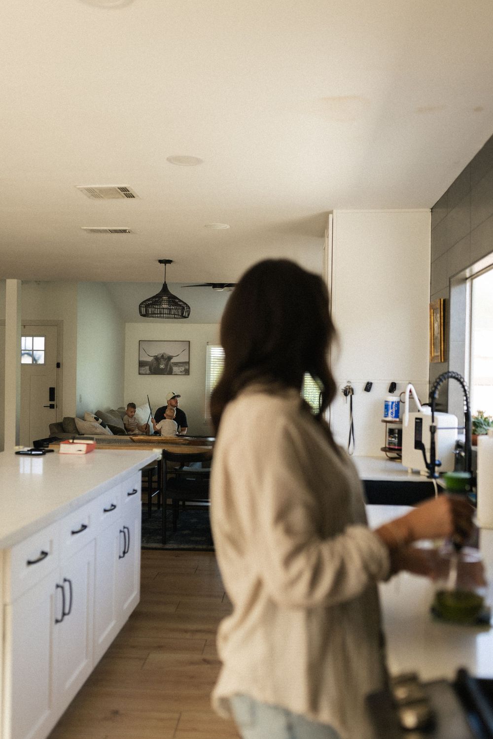 Person in beige sweater preparing food in a modern white kitchen with hardwood floors.