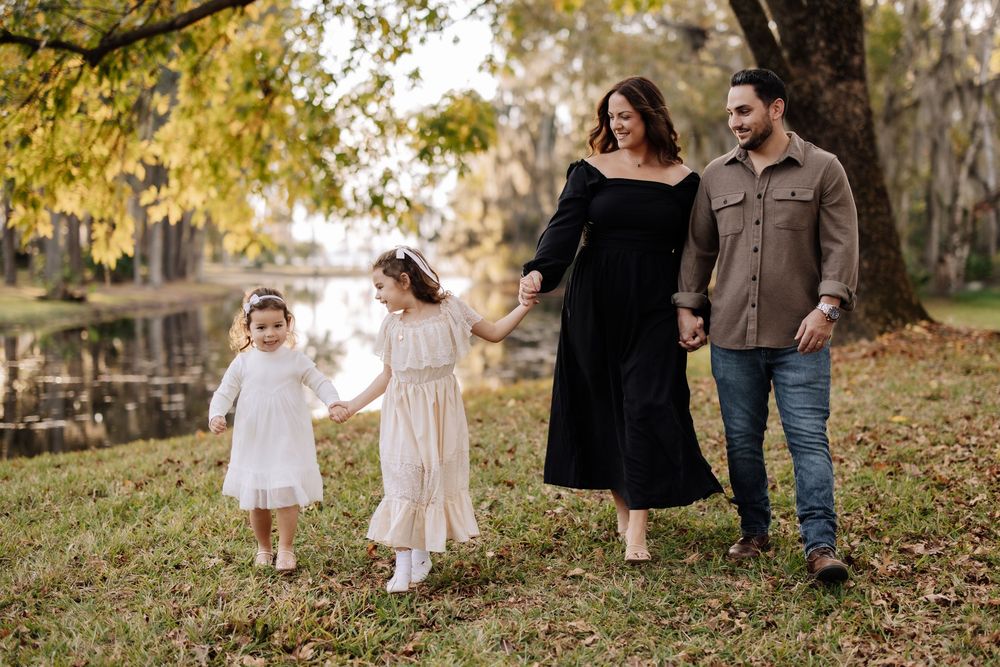 Family walking together through a scenic autumn park with fallen leaves during a golden hour photo session.