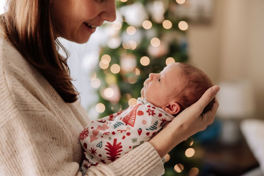 A tender moment between parent and newborn baby in front of a Christmas tree with soft bokeh lights in the background.