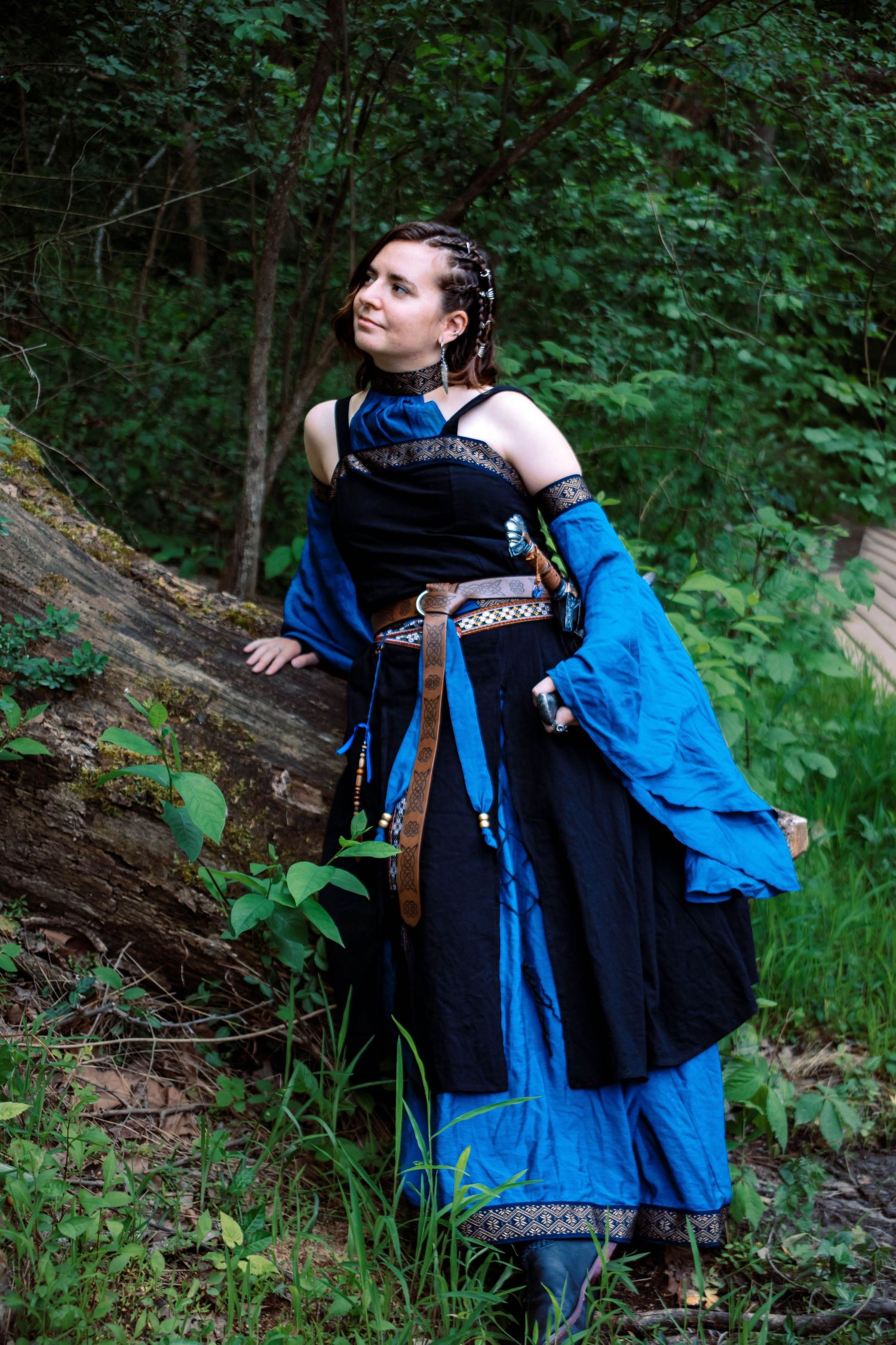 Medieval fantasy cosplay costume featuring a flowing black and bright blue dress with ornate details in a forest setting.