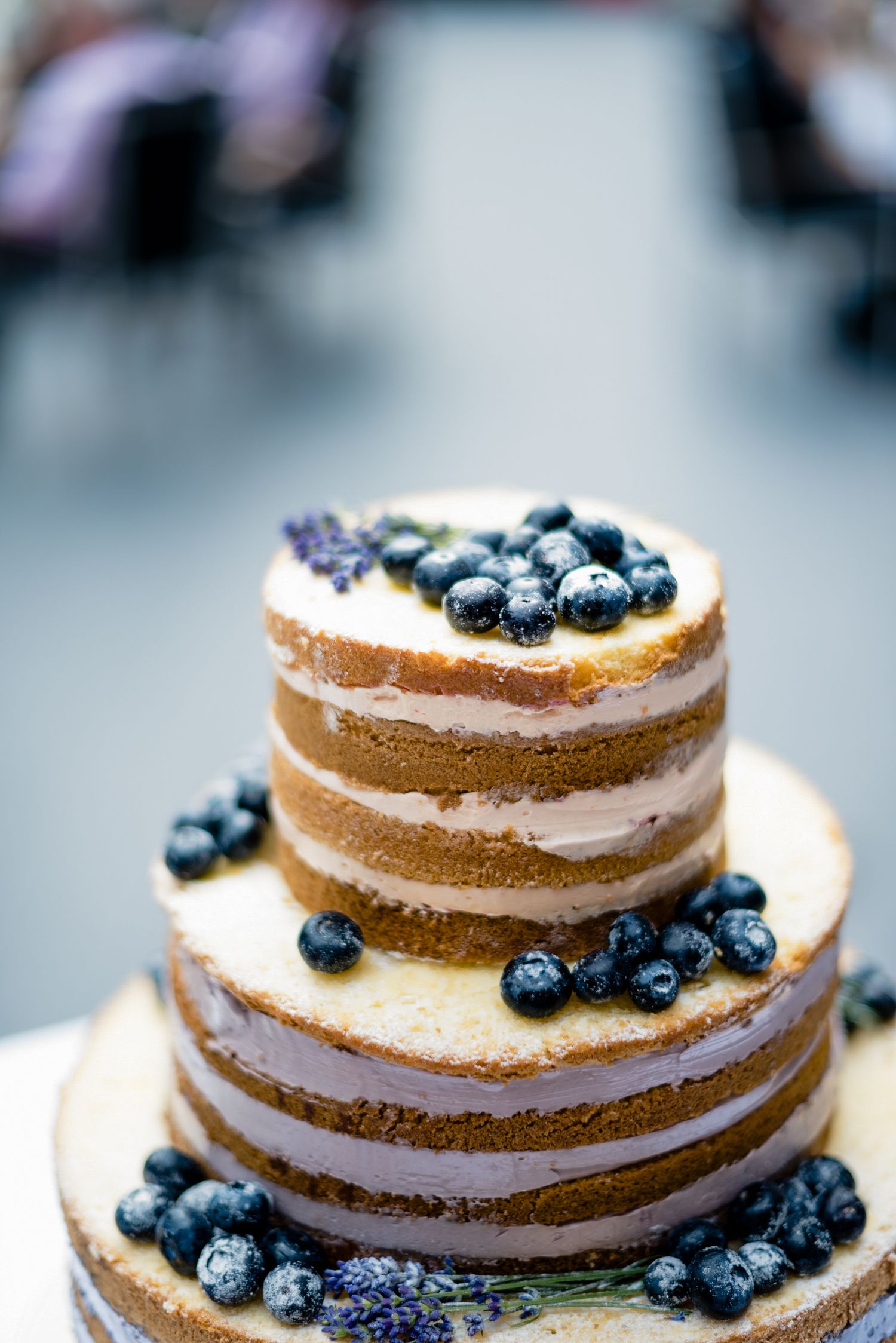 Dreistöckige Naked Cake mit Blaubeeren und Lavendel dekoriert, auf einem Tisch in einem festlichen Ambiente.