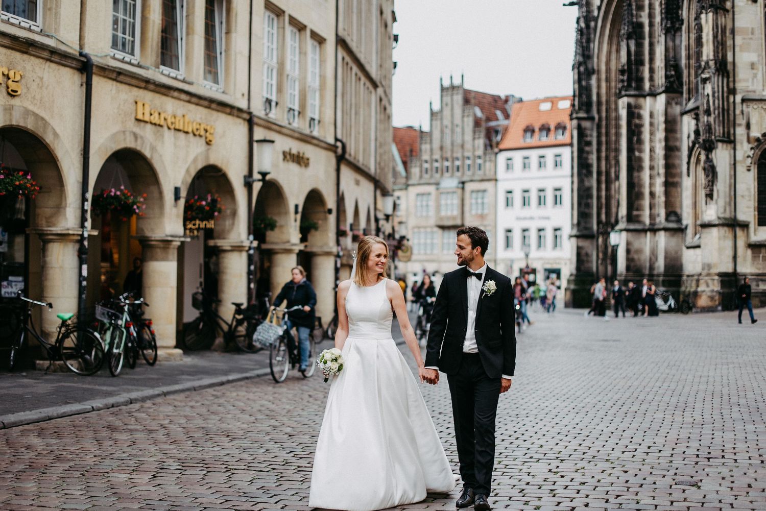 Ein Brautpaar läuft händelhaltend über den Münsteraner Prinzipalmarkt.