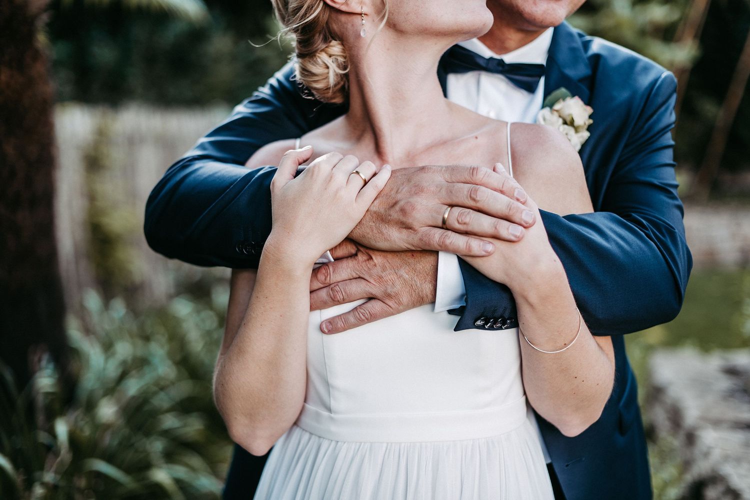 Ein Paar in eleganter Kleidung umarmt sich liebevoll im Freien. Die Frau trägt ein weißes Kleid, der Mann einen Anzug.