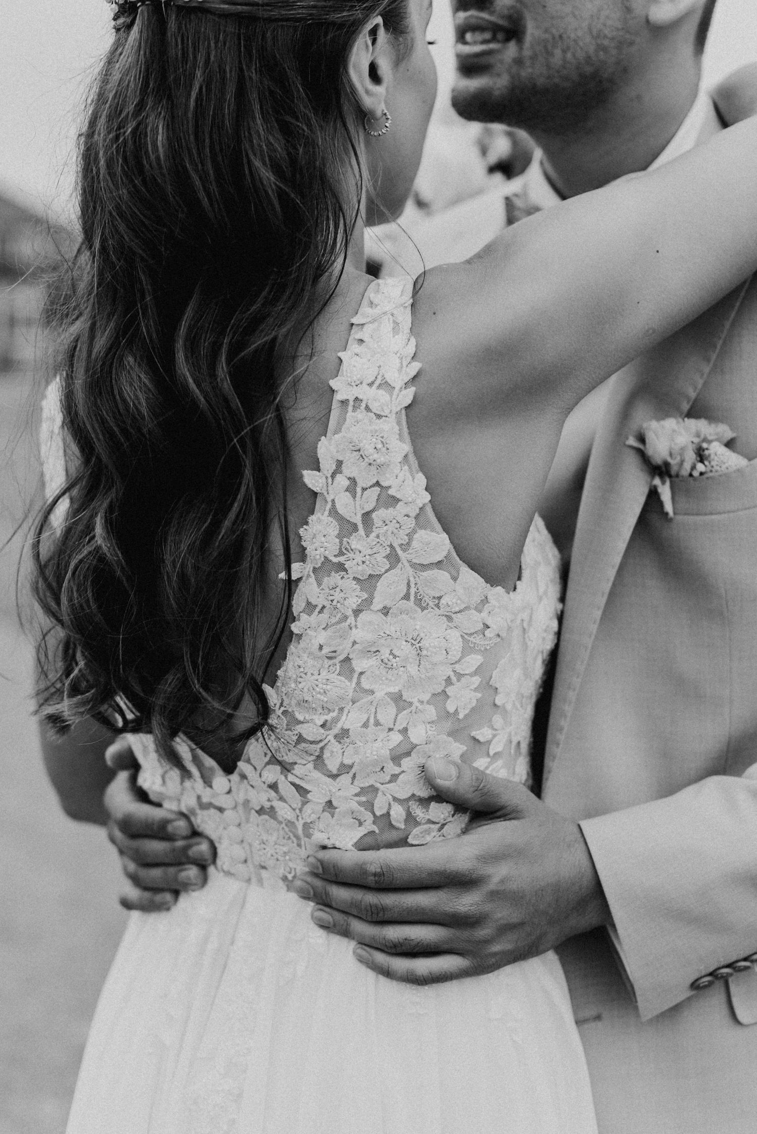 Schwarz-Weiß-Foto eines Hochzeitspaares in inniger Umarmung. Brautkleid mit Spitzenmuster, Bräutigam im Anzug.