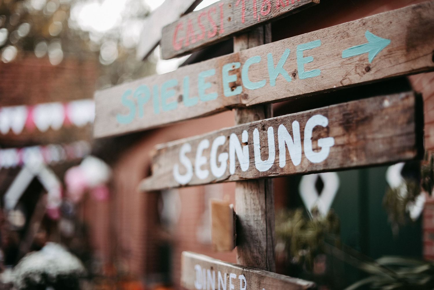 Holzschilder mit den Aufschriften "Spielecke" und "Segnung" zeigen in verschiedene Richtungen, im Hintergrund unscharfe Dekoration.