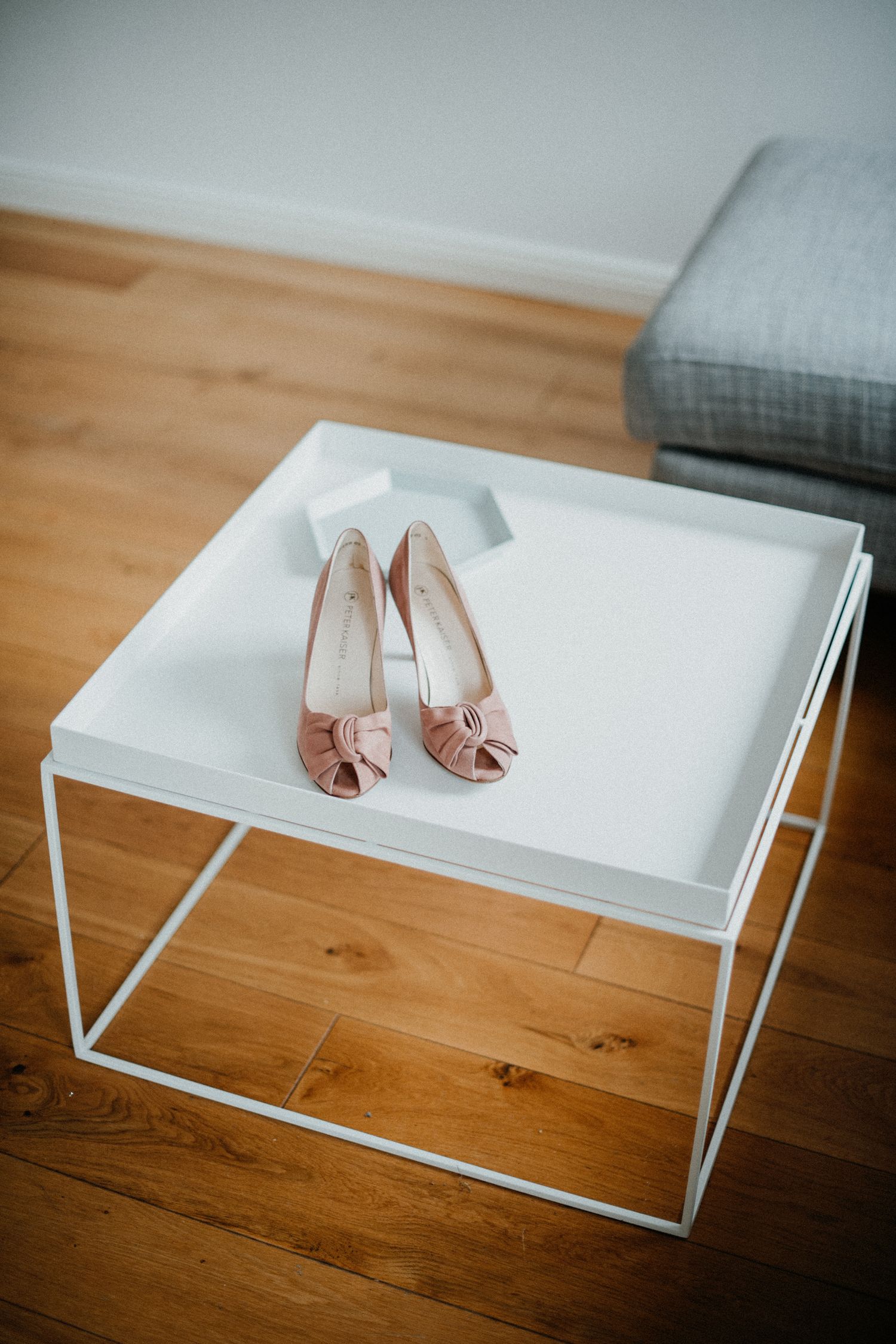 Ein Paar rosa High Heels steht auf einem weißen, quadratischen Tisch mit Holzfußboden im Hintergrund.