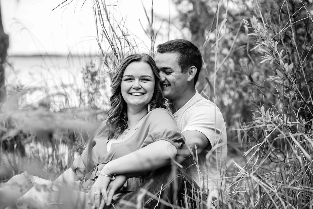 A romantic black and white portrait of a couple embracing outdoors among tall grass and plants.