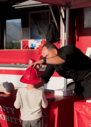 A person in black uniform helps a young child wearing a red cap at a red-painted concession stand window.