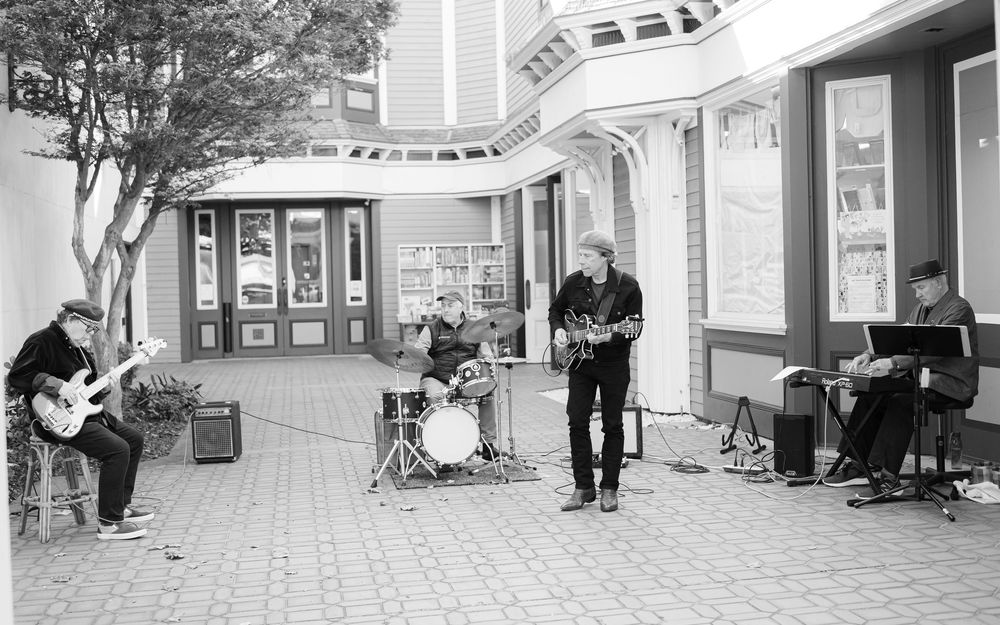 Black and white photo of a street band performing outdoors with guitars and drums by a building entrance.