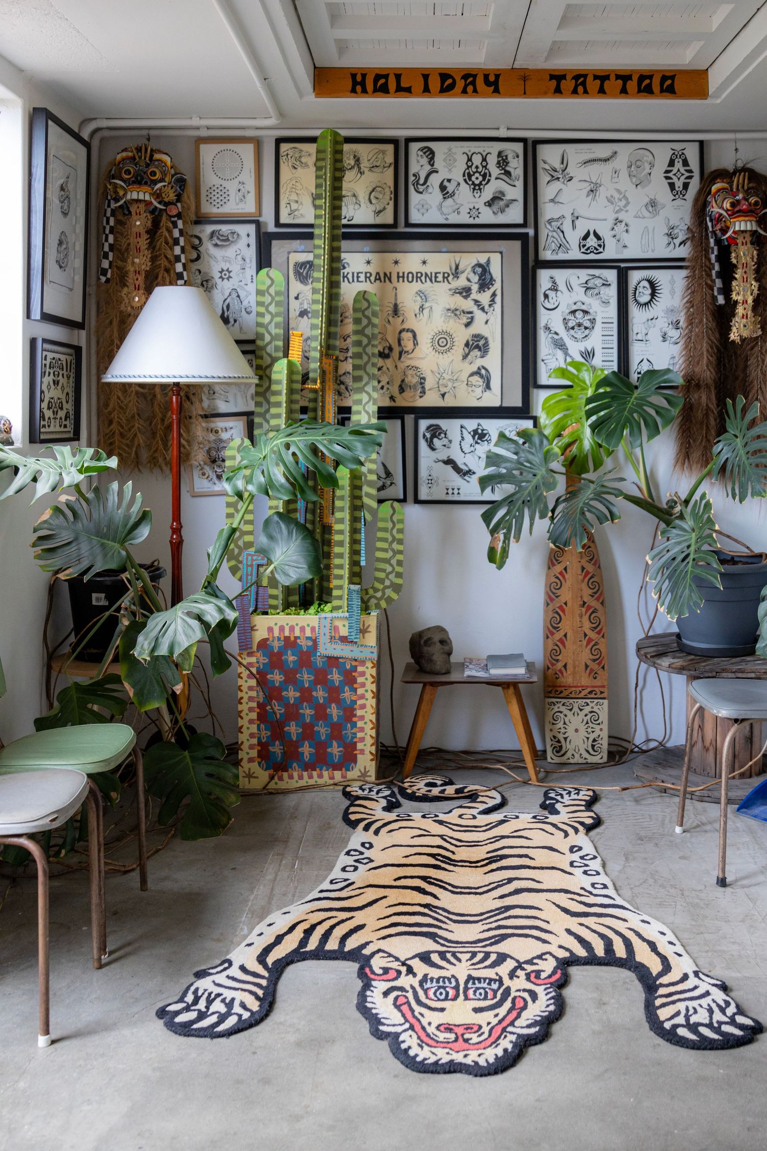 Tattoo studio with a bold tiger rug, eclectic décor, and walls filled with framed flash art and lush indoor plants.