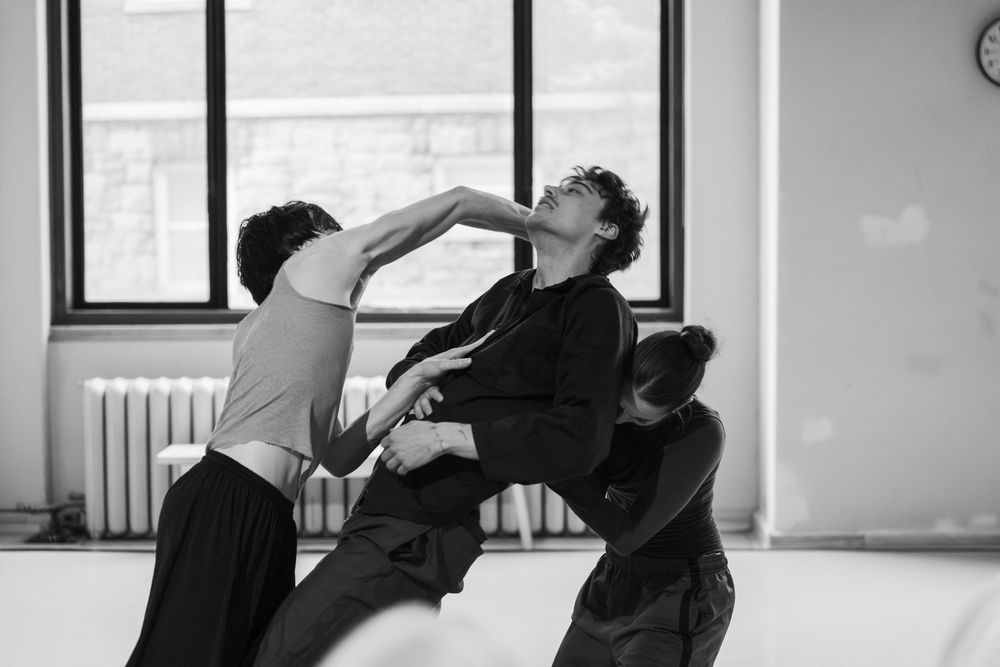 Dancers in a studio perform an expressive contemporary dance movement in black and white.
