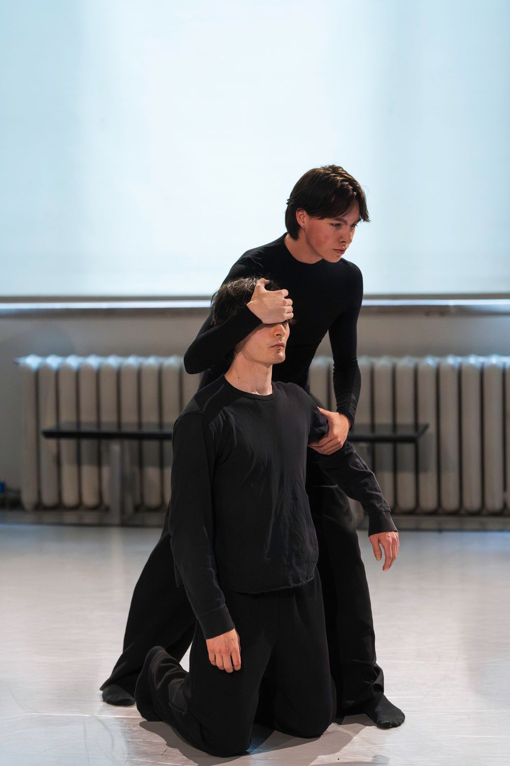 Two dancers in black outfits rehearse a contemporary performance piece in a bright dance studio.