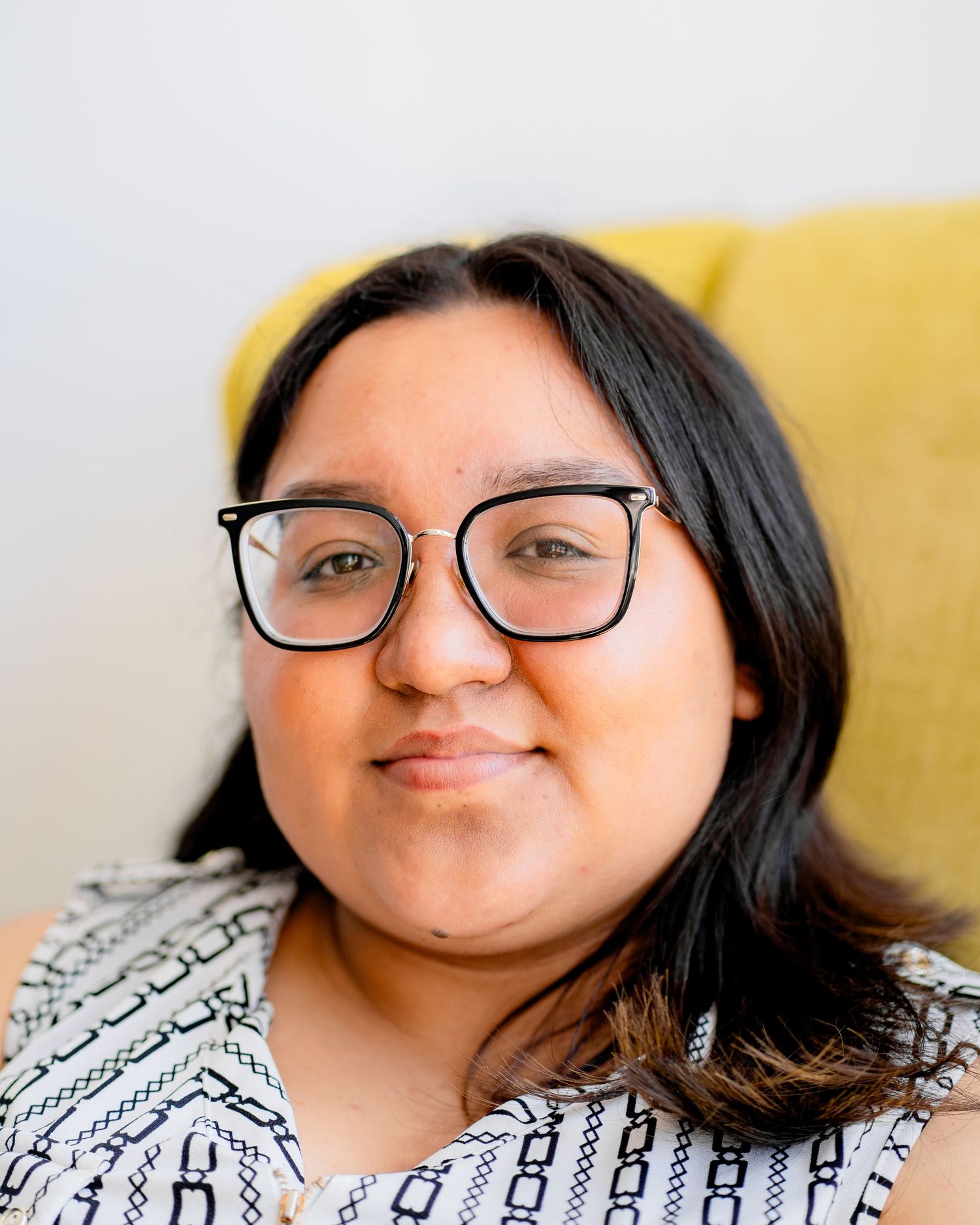 Portrait of a person in glasses smiling warmly against a yellow background.