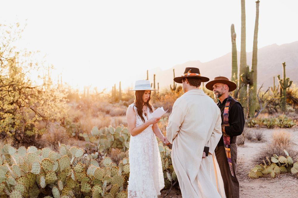 An intimate desert wedding ceremony takes place at sunset among towering saguaro cacti and prickly pear in Arizona.