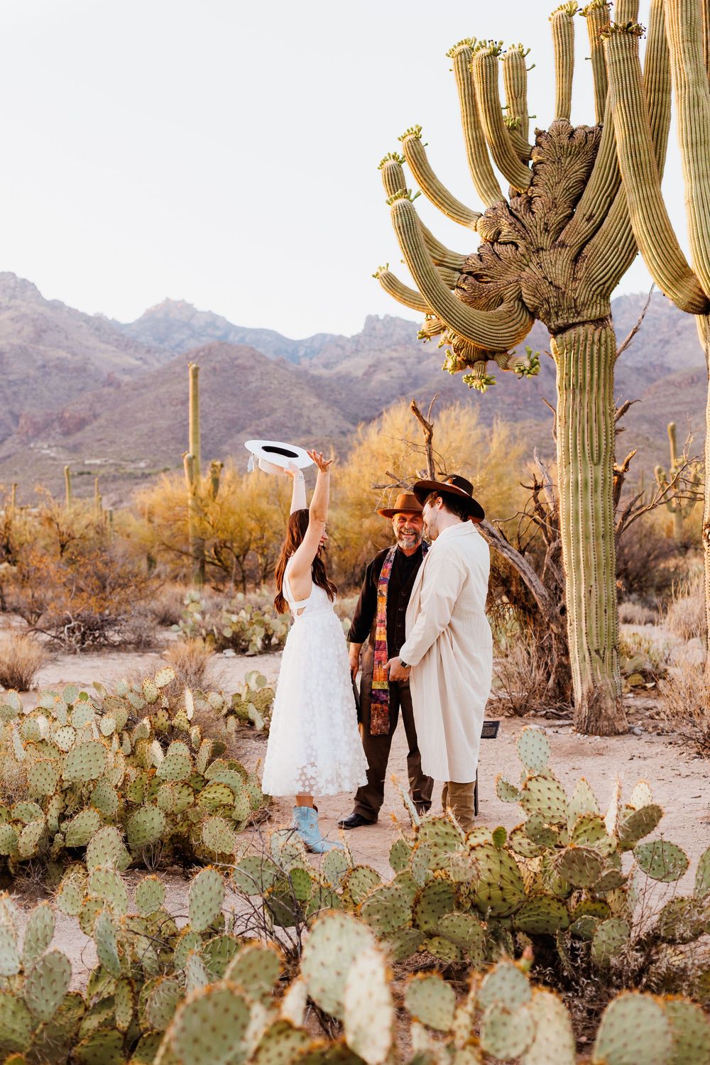 A couple celebrates joyfully beneath giant saguaro cacti in the desert during their intimate wedding ceremony.