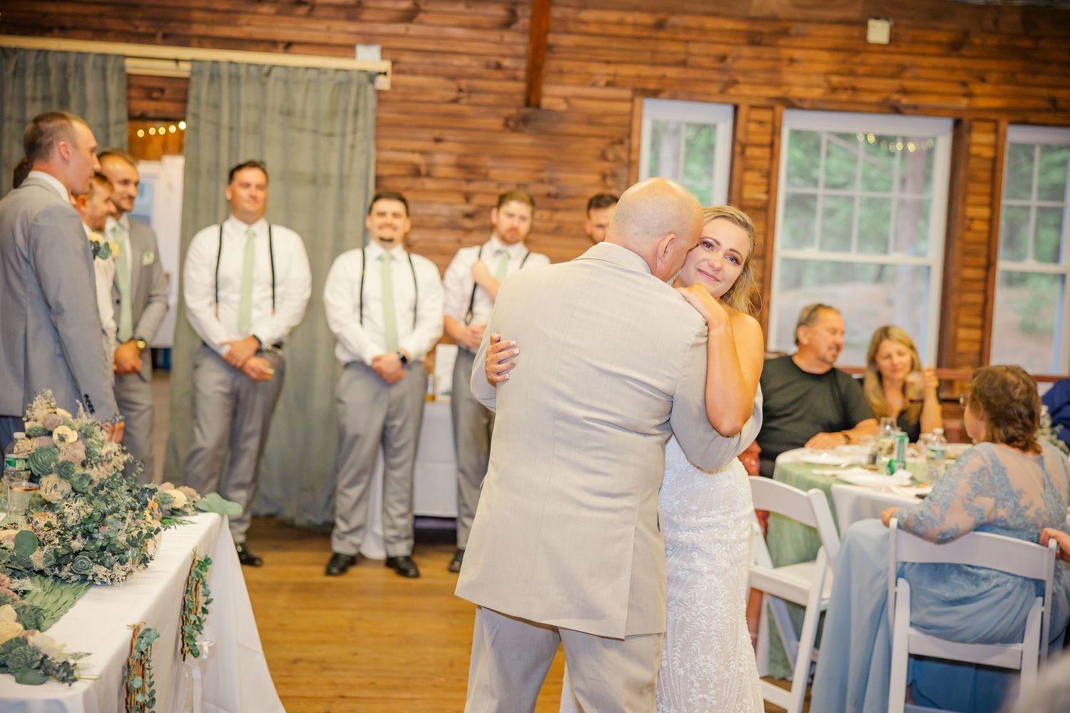 A couple shares their first dance at a rustic barn wedding reception while guests watch from the sidelines.
