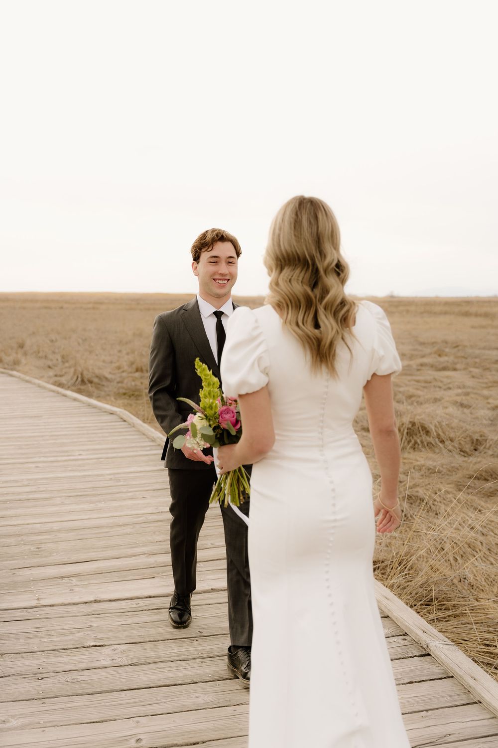 Wedding couple sharing a joyful moment on wooden boardwalk surrounded by rustic prairie landscape.