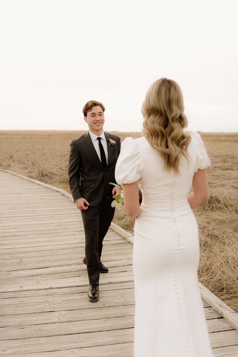 A couple shares a playful moment on a wooden boardwalk surrounded by prairie grass.