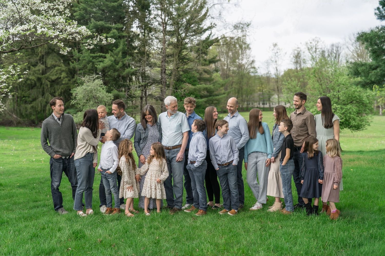 A large group standing together in a green field surrounded by trees on a spring day.