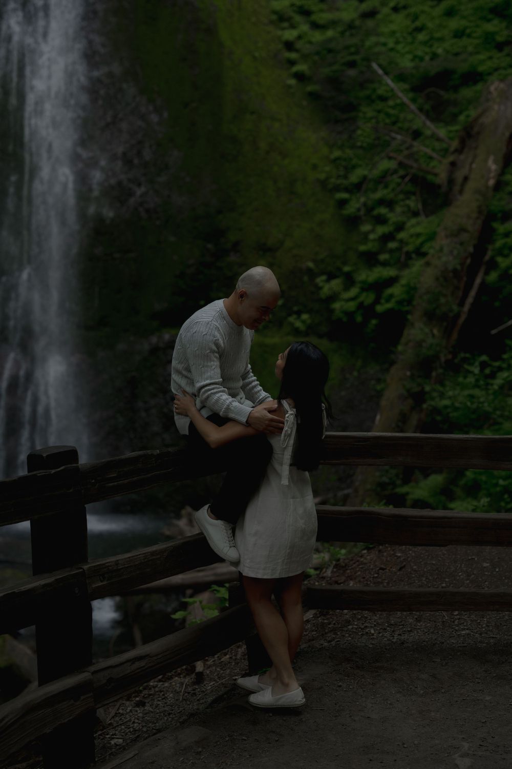 A couple shares a romantic moment on a wooden bridge by a cascading waterfall Marymere falls in Olympic National Park..