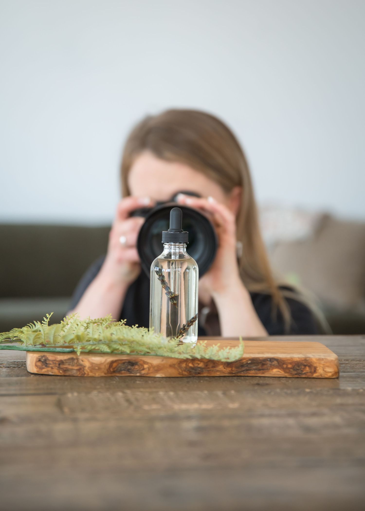 Photographer arranges white flowers on wooden table with camera nearby for product photography setup.