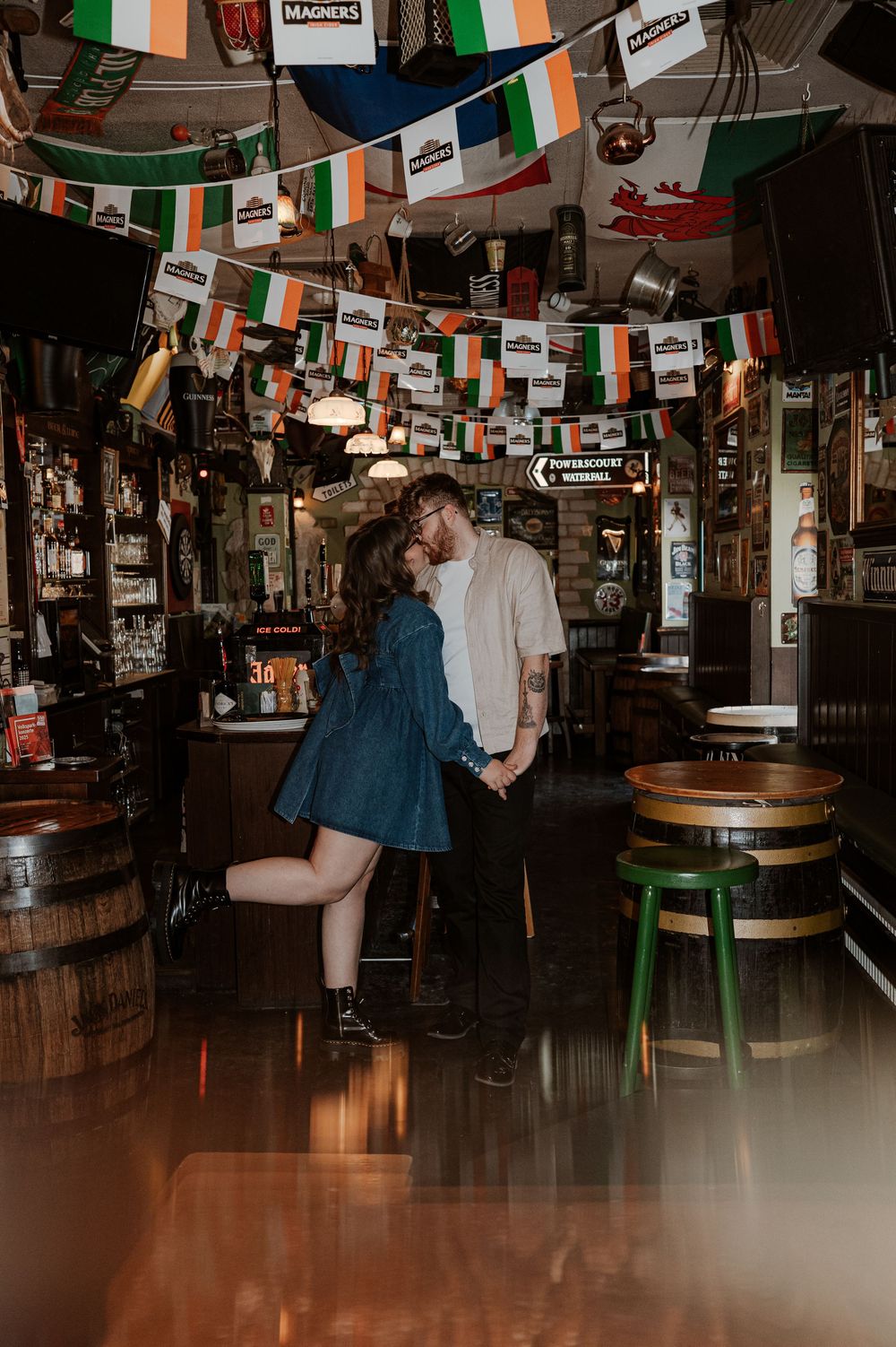 A couple dances together in a dimly lit Irish pub decorated with Irish flags and string lights.