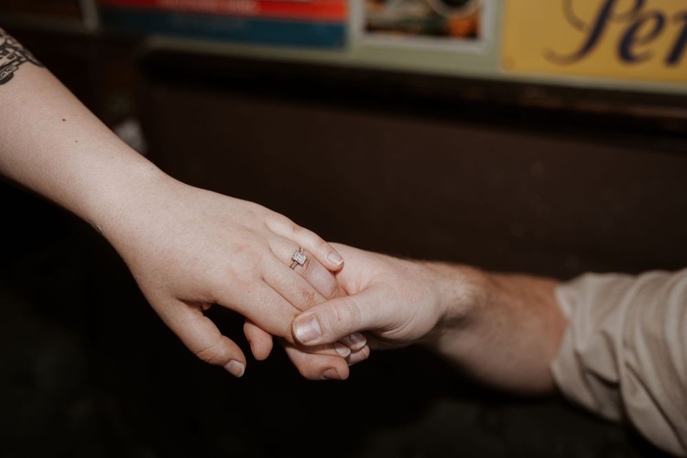 Two hands reach to hold each other intimately against a dark background with a wedding ring visible.