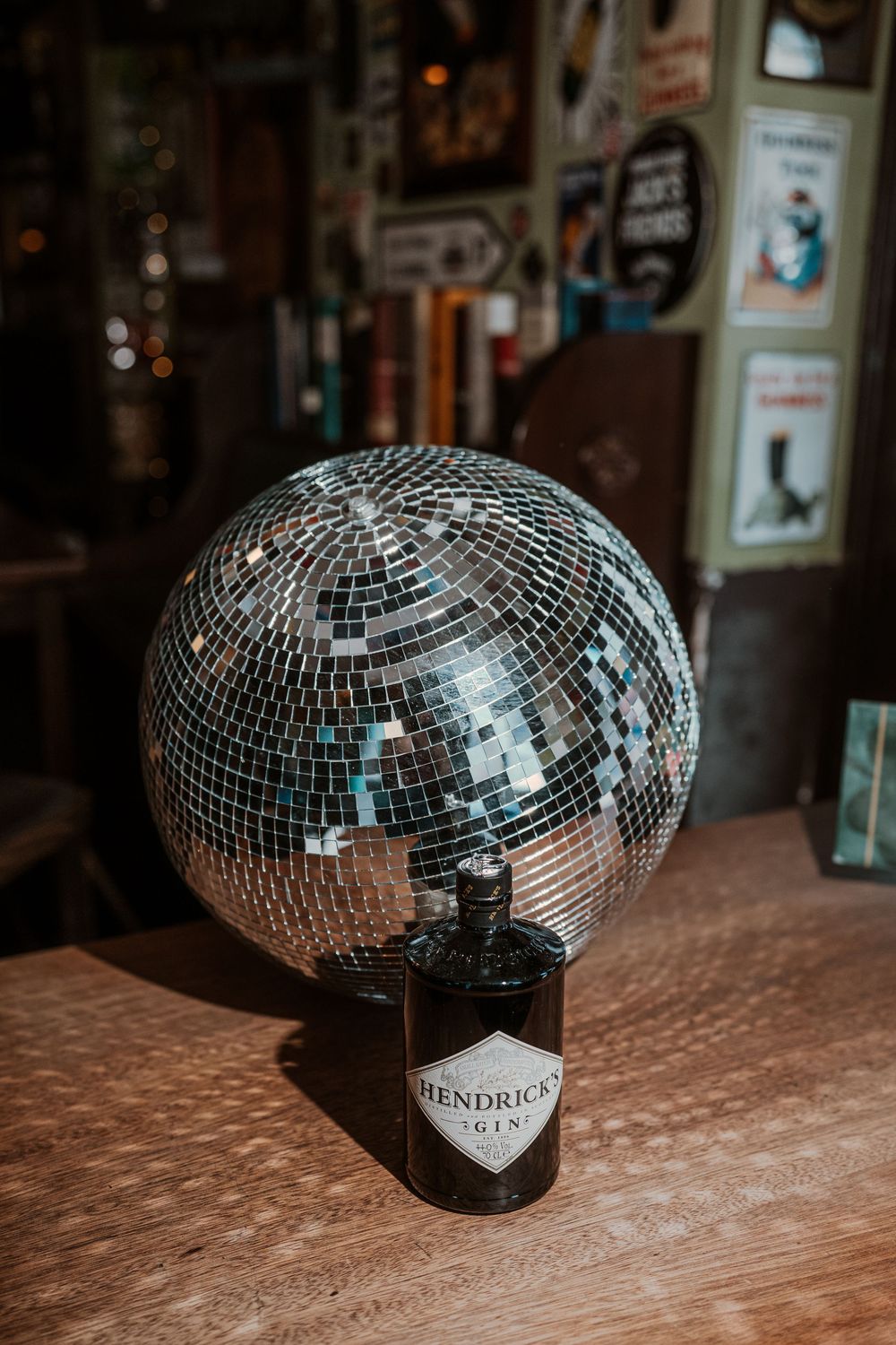 A shiny disco ball rests on top of a Hendricks gin bottle on a wooden surface in moody lighting.