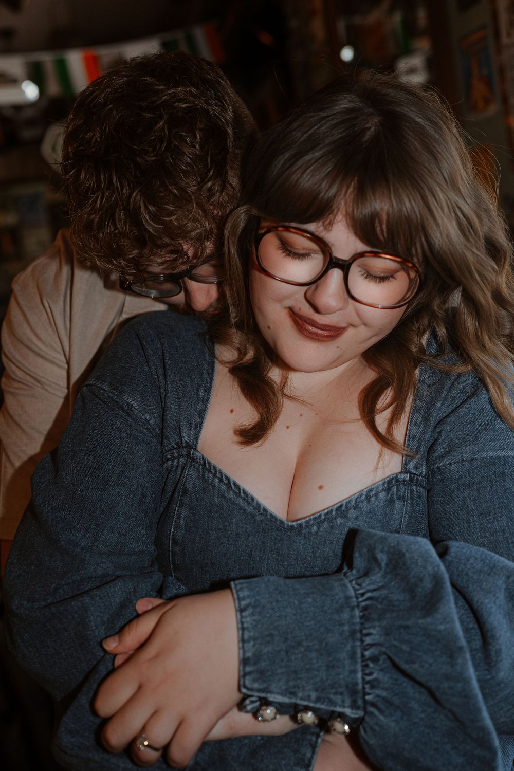 Intimate couple sharing tender moment in warm lighting while wearing denim and glasses.