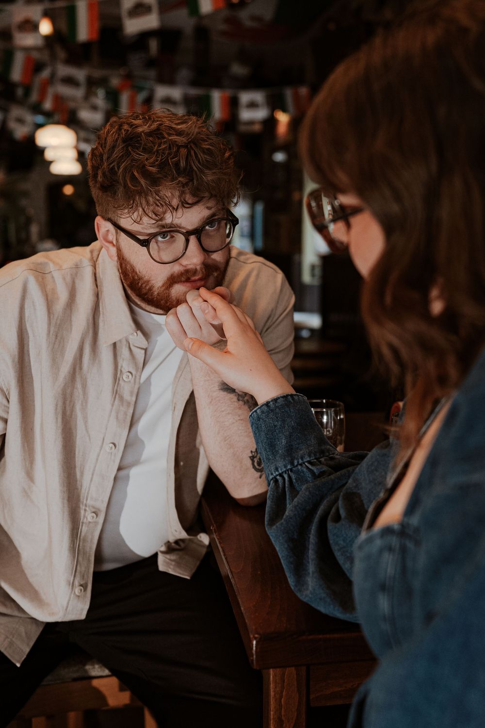 Two people in casual attire sit engaged in conversation at a dimly lit restaurant table.