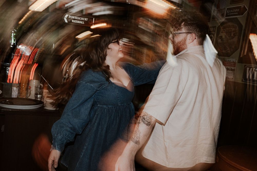 Two people dancing in a dimly lit, rustic bar setting with motion blur and vintage atmosphere.
