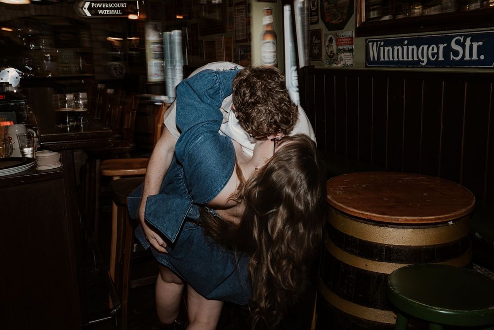 A couple share an intimate romantic moment inside a dimly lit bar setting.