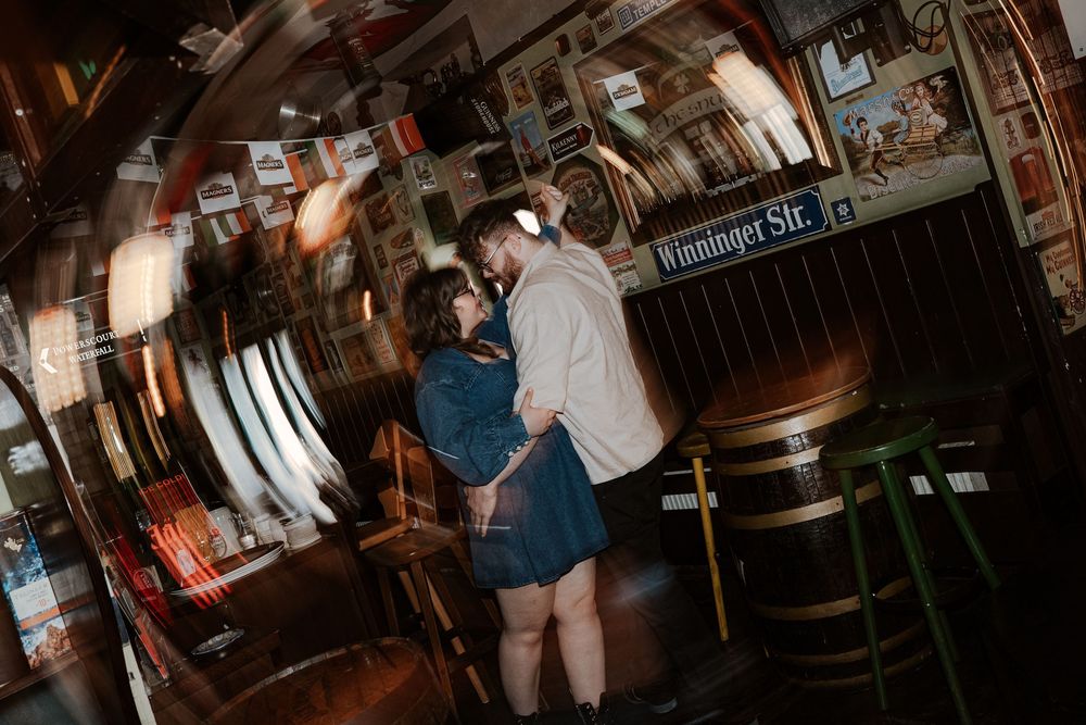 Customers gather at a dimly lit traditional pub bar with wooden fixtures and warm lighting creating a cozy atmosphere.