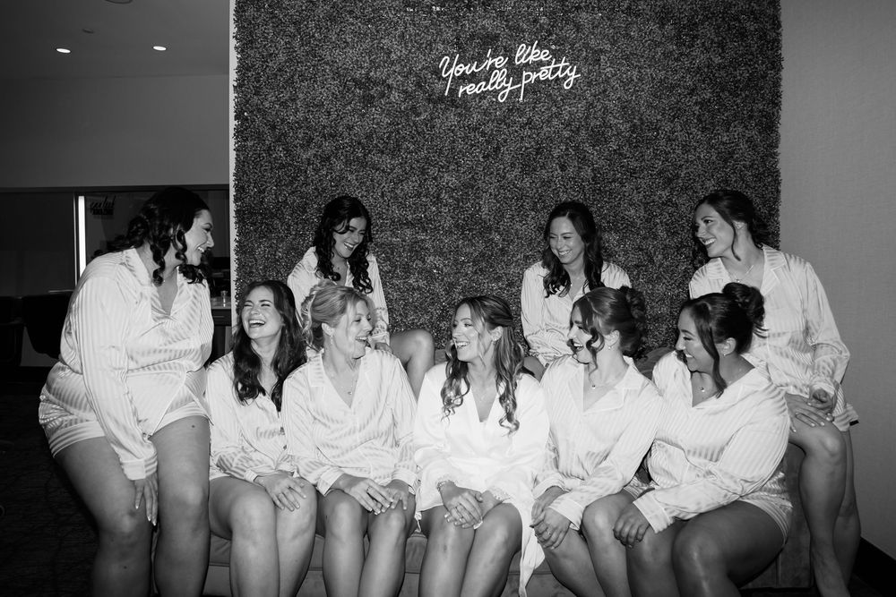 A black and white photograph shows a group of friends sitting together in white robes beneath a neon sign on the wall.